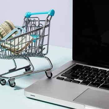 small shopping cart with cash beside a laptop